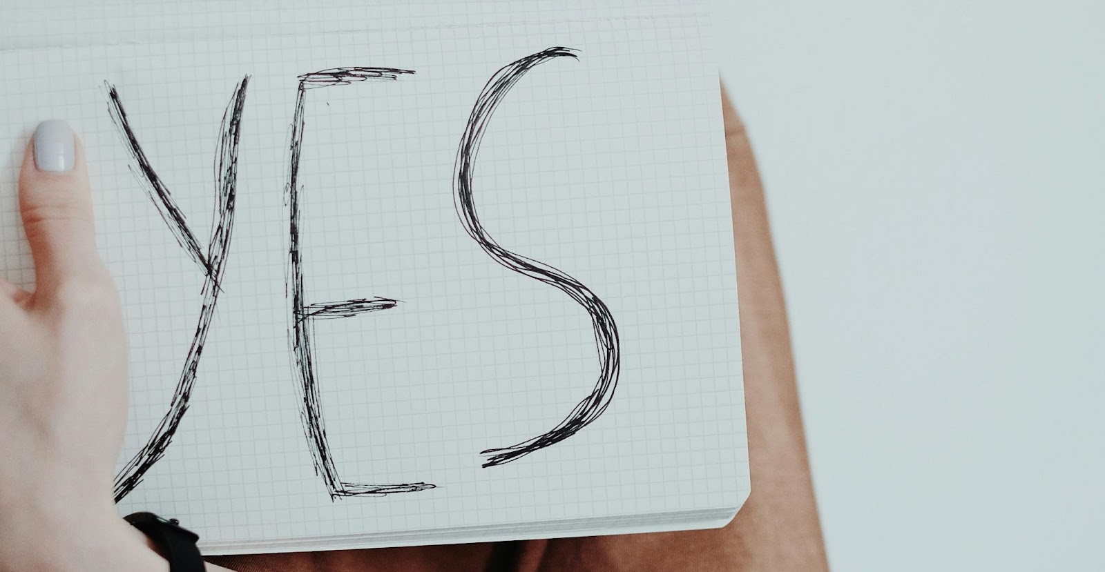 A person holding up a notebook with the word ‘yes’ on it.